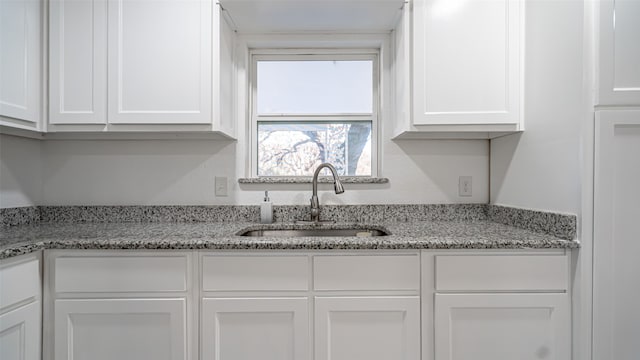 kitchen featuring light stone countertops, white cabinets, and sink