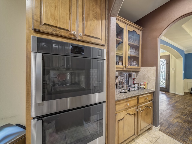 kitchen featuring light stone counters, tasteful backsplash, light hardwood / wood-style flooring, crown molding, and double oven