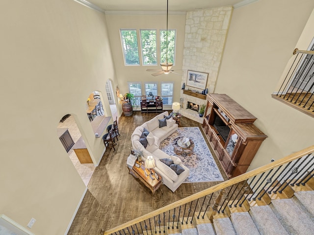 living room featuring ceiling fan, crown molding, hardwood / wood-style floors, and a stone fireplace