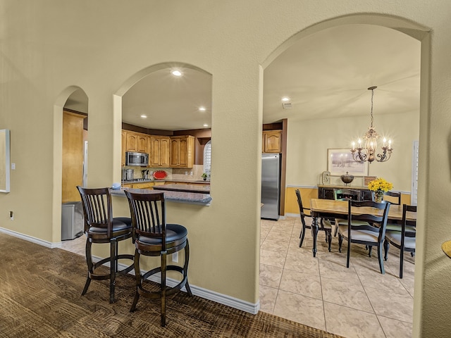 kitchen with pendant lighting, light tile patterned flooring, kitchen peninsula, appliances with stainless steel finishes, and an inviting chandelier