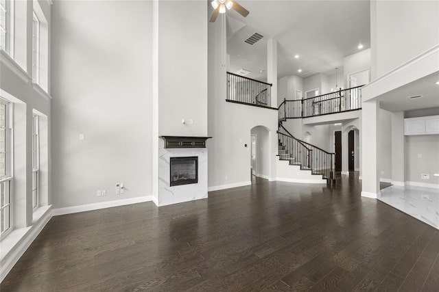 unfurnished living room with a high ceiling, dark wood-type flooring, and ceiling fan