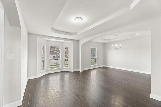 unfurnished living room with a notable chandelier, a raised ceiling, and dark hardwood / wood-style floors