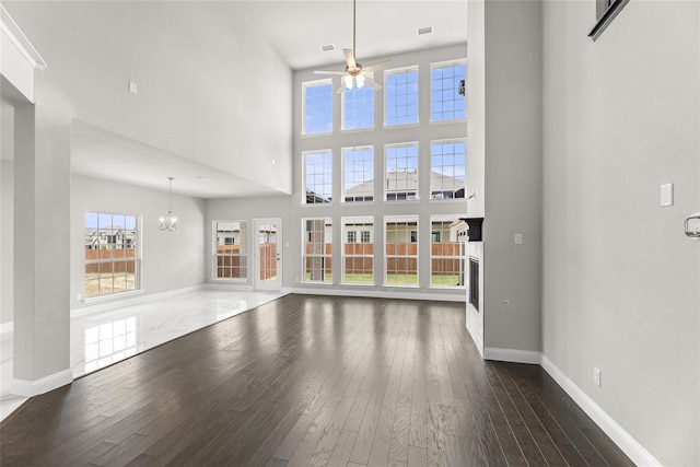 unfurnished living room featuring ceiling fan with notable chandelier, a high ceiling, and dark hardwood / wood-style flooring