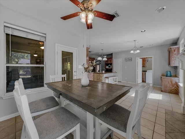 dining space featuring ceiling fan with notable chandelier, light tile patterned floors, and washing machine and clothes dryer