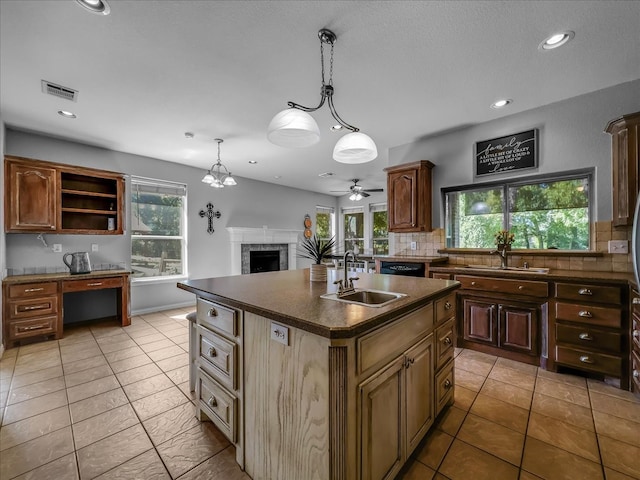 kitchen featuring a brick fireplace, an island with sink, backsplash, and a wealth of natural light