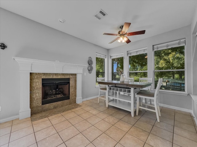 unfurnished dining area with ceiling fan, a tiled fireplace, and light tile patterned floors