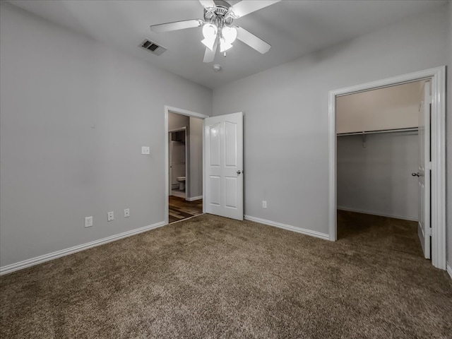 unfurnished bedroom with ceiling fan, a closet, dark colored carpet, and a spacious closet