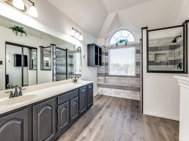 bathroom with vanity, lofted ceiling, a textured ceiling, a tile shower, and hardwood / wood-style flooring