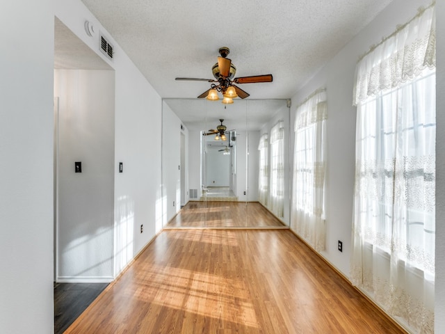 unfurnished room featuring wood-type flooring, ceiling fan, plenty of natural light, and a textured ceiling