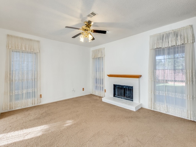 unfurnished living room featuring carpet, ceiling fan, a fireplace, and a textured ceiling