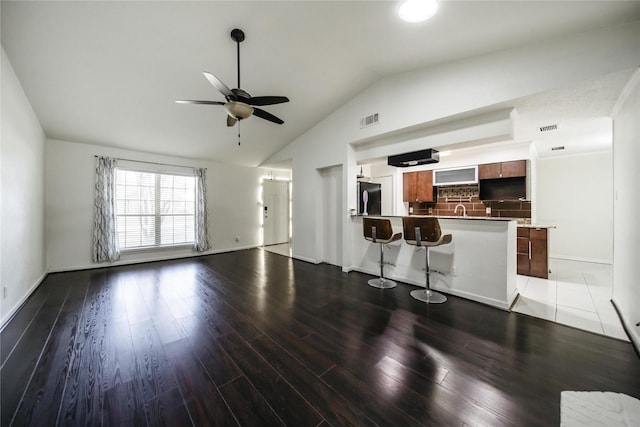 kitchen featuring backsplash, a breakfast bar, vaulted ceiling, ceiling fan, and fridge