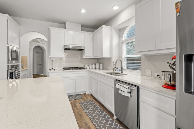 kitchen featuring stainless steel appliances, white cabinetry, light stone counters, and sink