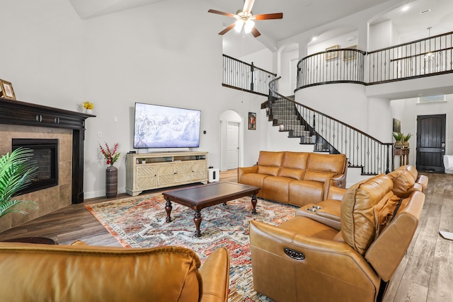 living room featuring a tile fireplace, hardwood / wood-style flooring, ceiling fan, and high vaulted ceiling