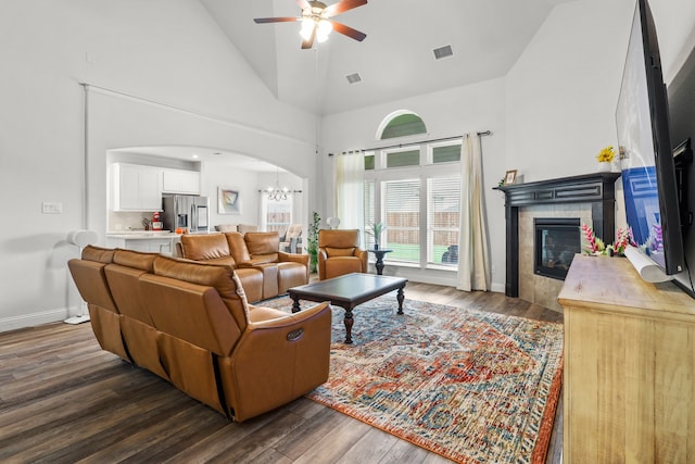 living room featuring ceiling fan with notable chandelier, a fireplace, dark hardwood / wood-style flooring, and high vaulted ceiling