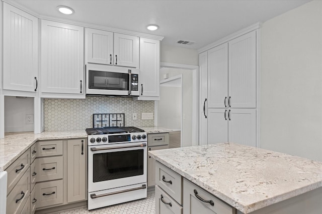 kitchen featuring backsplash, white cabinets, light stone countertops, high end stove, and light tile patterned flooring