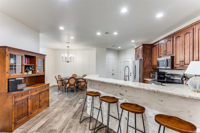 kitchen featuring light hardwood / wood-style flooring, stainless steel appliances, an inviting chandelier, decorative light fixtures, and light stone countertops