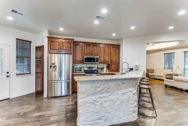 kitchen featuring light stone countertops, dark hardwood / wood-style flooring, stainless steel appliances, a kitchen bar, and sink