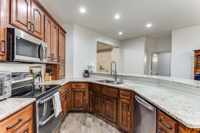 kitchen featuring sink, kitchen peninsula, light hardwood / wood-style flooring, stainless steel appliances, and light stone countertops