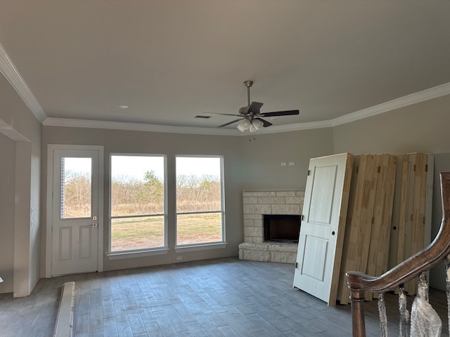 unfurnished living room with ceiling fan, plenty of natural light, a fireplace, and ornamental molding