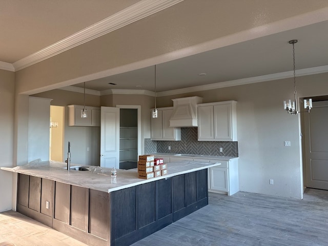 kitchen featuring white cabinetry, sink, premium range hood, decorative light fixtures, and decorative backsplash