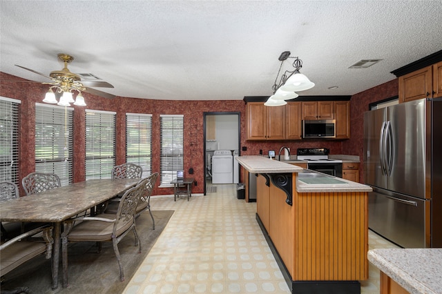 kitchen featuring a textured ceiling, a kitchen island, appliances with stainless steel finishes, decorative light fixtures, and ceiling fan