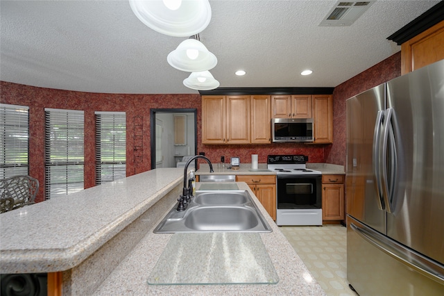 kitchen with a textured ceiling, stainless steel appliances, hanging light fixtures, and sink