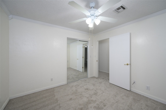 empty room with a textured ceiling, light colored carpet, ceiling fan, and crown molding