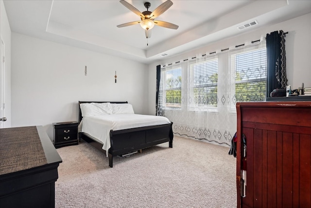 carpeted bedroom with ceiling fan and a tray ceiling