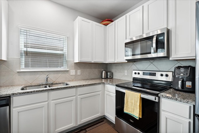 kitchen with appliances with stainless steel finishes, light stone counters, white cabinets, backsplash, and sink