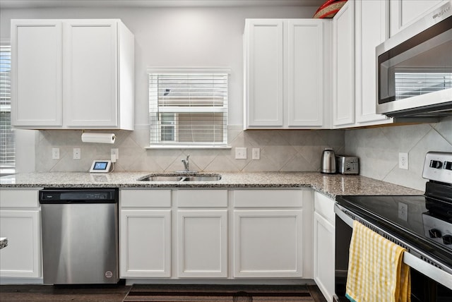 kitchen featuring appliances with stainless steel finishes, white cabinetry, backsplash, light stone countertops, and sink