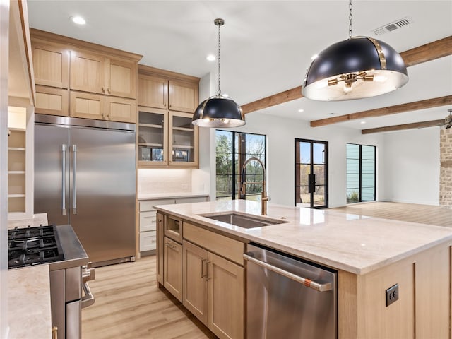 kitchen featuring sink, stainless steel appliances, beamed ceiling, light brown cabinetry, and a center island with sink