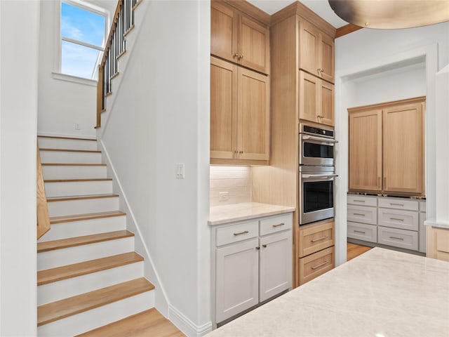 kitchen with tasteful backsplash, light brown cabinetry, stainless steel double oven, and light hardwood / wood-style floors