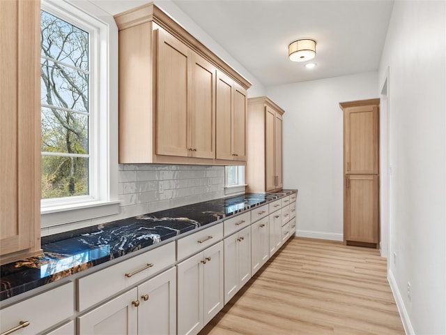 kitchen featuring decorative backsplash, light hardwood / wood-style flooring, plenty of natural light, and dark stone countertops