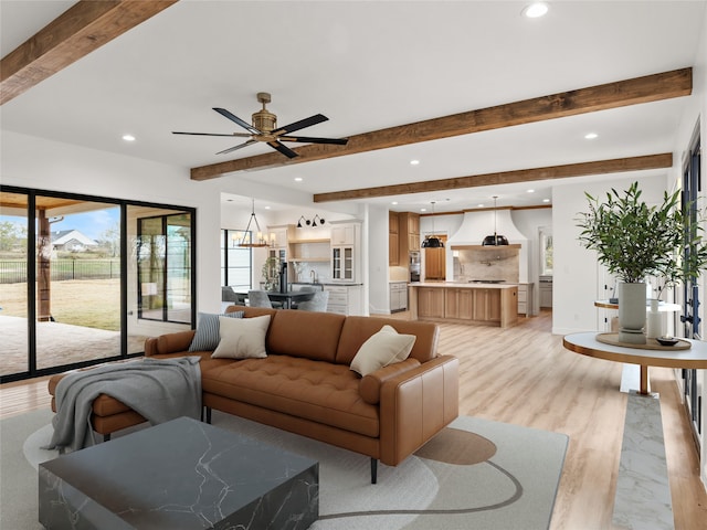 living room featuring ceiling fan with notable chandelier, beam ceiling, and light hardwood / wood-style flooring