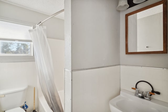 full bathroom with tile walls, a textured ceiling, sink, shower / tub combo, and toilet