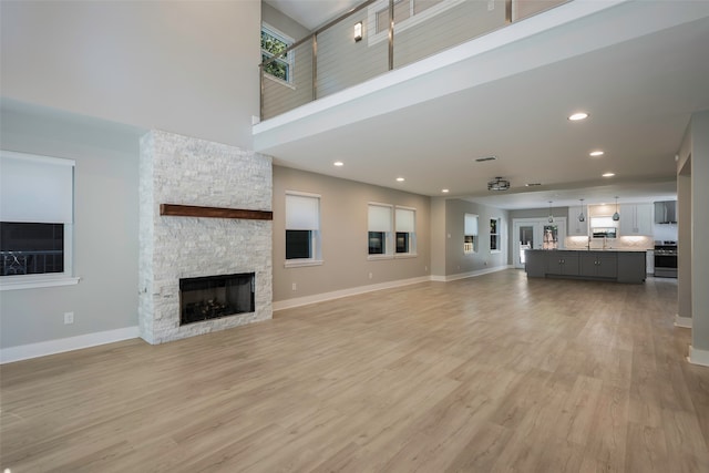 unfurnished living room featuring a towering ceiling, light wood-type flooring, and a fireplace