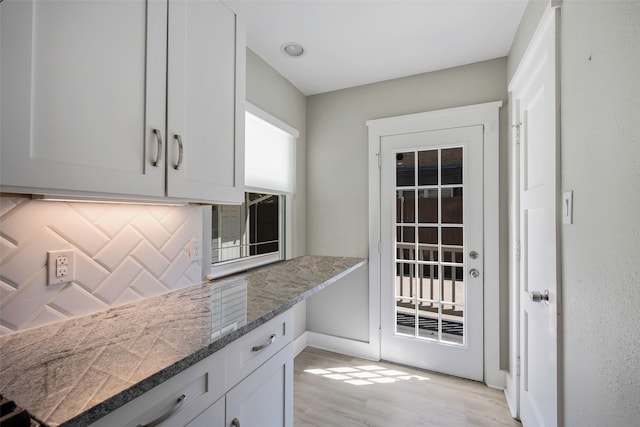 kitchen with dark stone counters, light hardwood / wood-style floors, white cabinetry, and tasteful backsplash