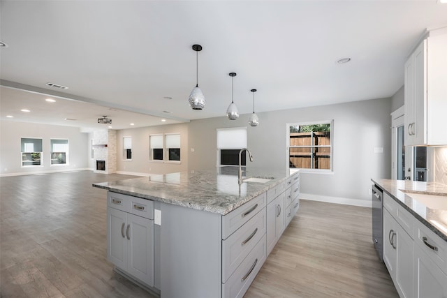 kitchen featuring an island with sink, sink, decorative light fixtures, a large fireplace, and light hardwood / wood-style floors