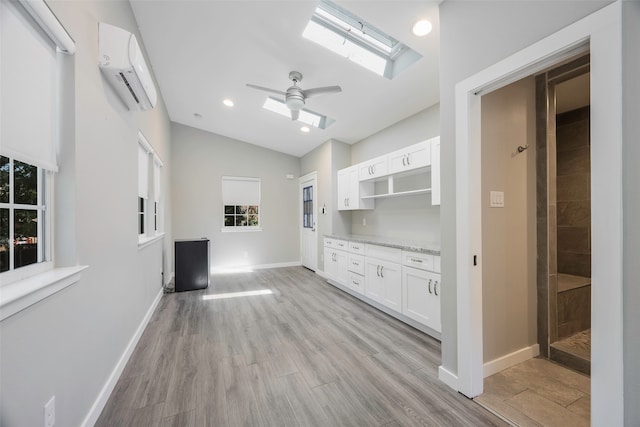 unfurnished living room with vaulted ceiling with skylight, light hardwood / wood-style floors, ceiling fan, and a healthy amount of sunlight