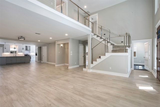 unfurnished living room with light hardwood / wood-style flooring, a towering ceiling, and sink