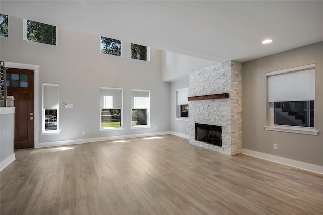 unfurnished living room with light wood-type flooring, a stone fireplace, and a towering ceiling