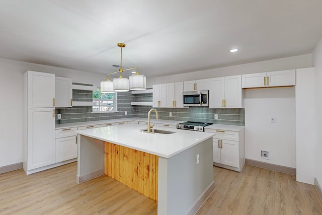 kitchen with appliances with stainless steel finishes, light hardwood / wood-style floors, an island with sink, white cabinets, and sink