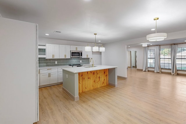 kitchen featuring sink, an island with sink, white cabinets, light hardwood / wood-style flooring, and decorative light fixtures