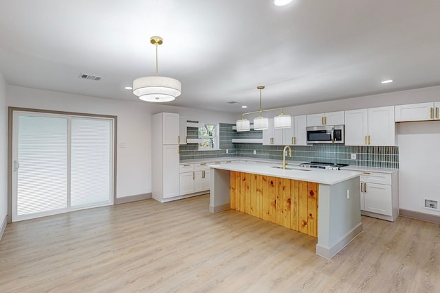 kitchen featuring light hardwood / wood-style floors, a kitchen island with sink, white cabinetry, backsplash, and decorative light fixtures