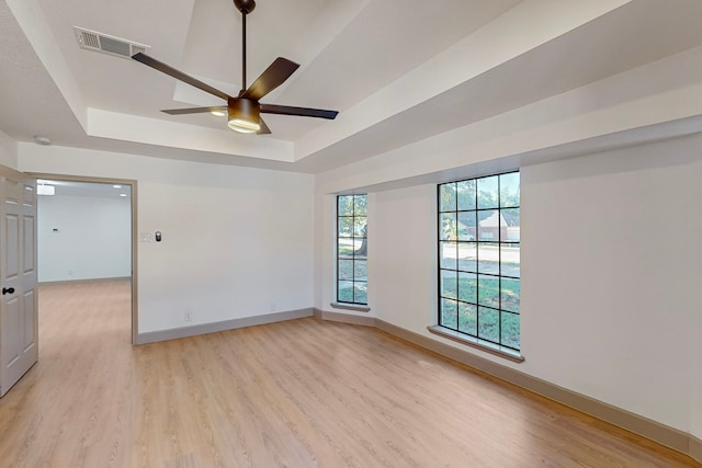 empty room featuring light wood-type flooring, ceiling fan, and a raised ceiling