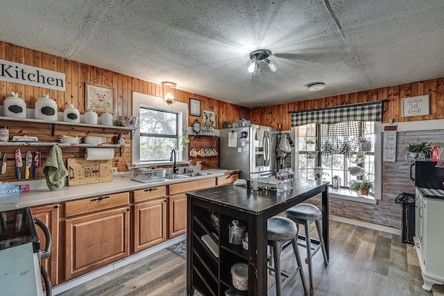 kitchen featuring wooden walls, hardwood / wood-style flooring, stainless steel fridge with ice dispenser, and sink