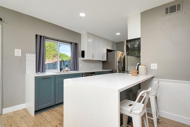 kitchen featuring light wood-type flooring, sink, kitchen peninsula, a kitchen breakfast bar, and stainless steel fridge