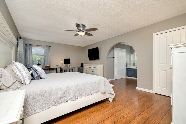 bedroom with connected bathroom, ceiling fan, hardwood / wood-style flooring, and a textured ceiling