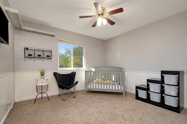 bedroom featuring light carpet, a textured ceiling, a nursery area, and ceiling fan