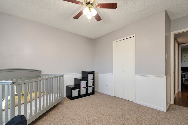 carpeted bedroom featuring ceiling fan, a textured ceiling, a closet, and a crib